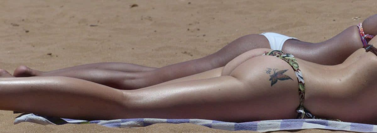 Two women sunbathing on the beach, wearing bikinis