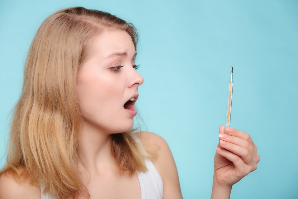 Sick girl with fever checking mercury thermometer on blue.