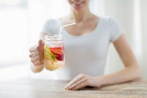 close up of happy woman holding glass with fruit water at home